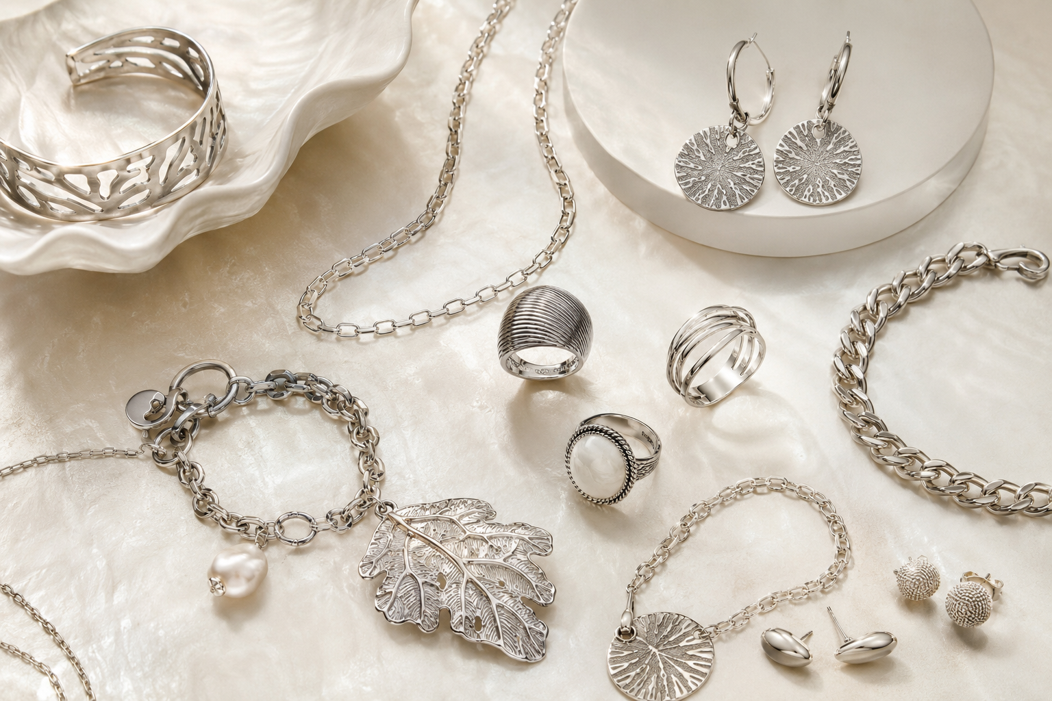 Elegant Made in Italy sterling silver jewelry including chains, rings, earrings, pendants and bracelets on a pearlescent surface.